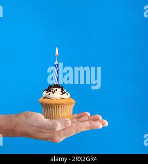 Hand holding a chocolate cupcake with a lit candle Stock Photo