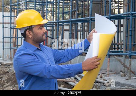 Professional engineer architect worker with protective helmet analyzing blueprint paper at house building construction site Stock Photo