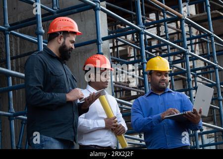 Three engineers from the Construction Industry Development Council members planning using laptop, blueprint and notepad at project site Stock Photo