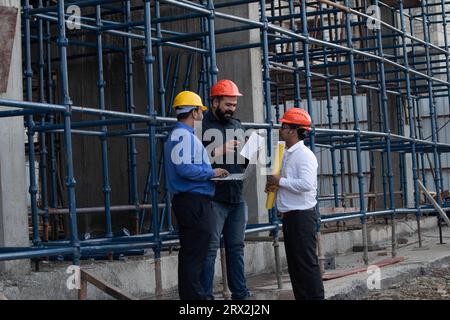 Team of three male construction engineers wearing safety hardhats planning and discussing at project site. Stock Photo