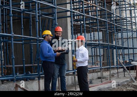 Team of three male construction engineers wearing safety hardhats planning and discussing next phase of construction at building project site. Stock Photo