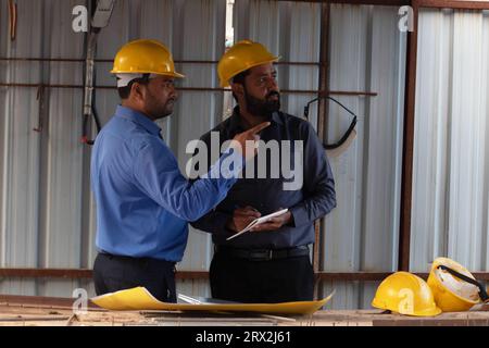 Two civil engineers planning at makeshift shelter of project site. Foreman showing colleague something at the construction site by pointing his finger Stock Photo