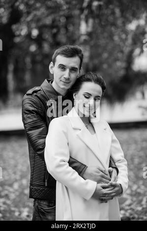 A man hugs his pregnant wife. A man in a black jacket hugs a woman in a white coat Stock Photo