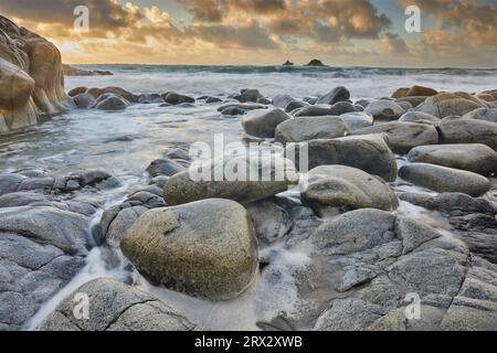 Atlantic rollers surge around shoreline granite boulders on a rising tide at sunset, Porth Nanven, a remote cove near St. Just Stock Photo