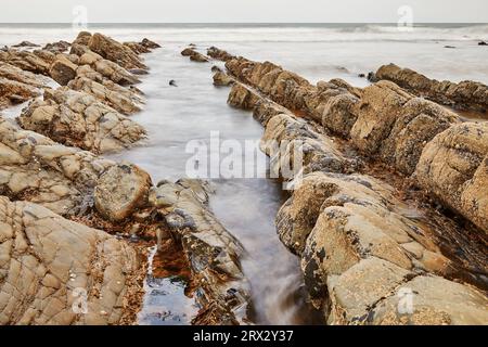 A rising tide brings the Atlantic around and over shoreline rocks at Welcombe Mouth, a remote cove near Hartland, on the Atlantic coast of Devon Stock Photo