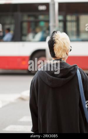 Young woman with alternative style waiting for the traffic light to turn green in Alicante and a bus passing in the background, Spain Stock Photo