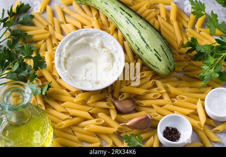 Food background. Penne pasta, zucchini, cream cheese, olive oil, parsley, garlic, salt and black pepper, top view. Ingredients for making vegetarian p Stock Photo