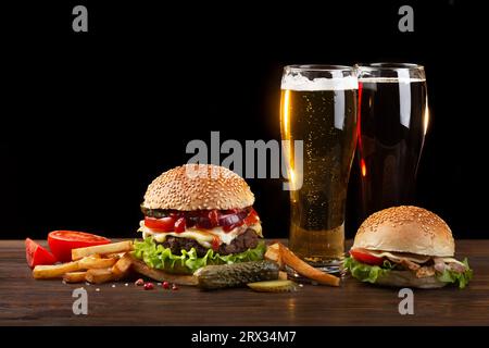 Homemade hamburger with french fries and two glasses of beer on wooden table. Fastfood on dark background. Stock Photo