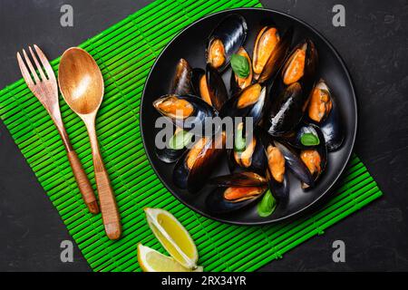 Seafood mussels and basil leaves in a black plate on bamboo mat and stone table. Top view. Stock Photo