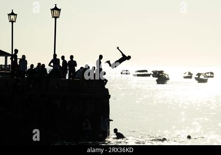 Silhouetted teenagers dive into the sea from the town pier, Stone Town, Zanzibar island, Tanzania, East Africa, Africa Stock Photo