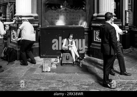 A Female Shoe Shiner Reads A Book Whilst Waiting For Customers, Leadenhall Market, City of London, London, UK. Stock Photo