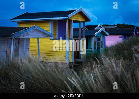 Colourful bathing huts in the sand dunes on the beach of Skanör  glow in the evening twilight against a dramatic cloudy sky, Skåne, Sweden Stock Photo