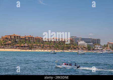 Mexico, Cabo San Lucas - July 16, 2023: Modern building complex El Medano Ejidal resort at Hacienda Beach under blue sky. Small pleasure boats on blue Stock Photo