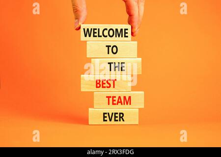 Welcome to best team symbol. Concept words Welcome to the best team ever on wooden block. Beautiful orange table background. Businessman hand. Busines Stock Photo