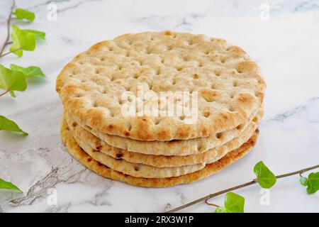 Greek style whole wheat pita bread on marble background with ivy sprigs in horizontal format.  Selective focus on front of stack of pitas. Stock Photo