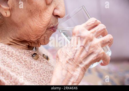 Old woman drinking water from glass cup Stock Photo