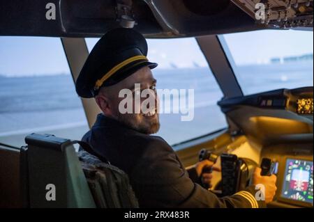 Caucasian bearded man smiling while sitting in a flight simulator. Pilot in the cockpit. Stock Photo