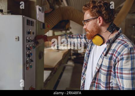 Professional carpenter in furniture factory pressing button on machine to start production Stock Photo