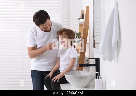 Father helping his son to brush teeth in bathroom Stock Photo