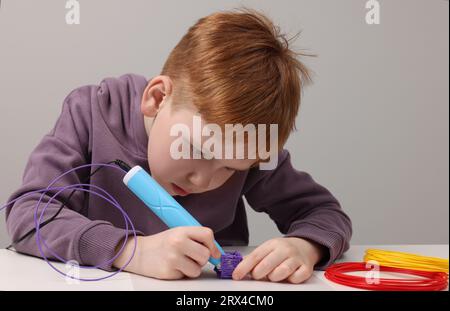Boy drawing with stylish 3D pen at white table Stock Photo