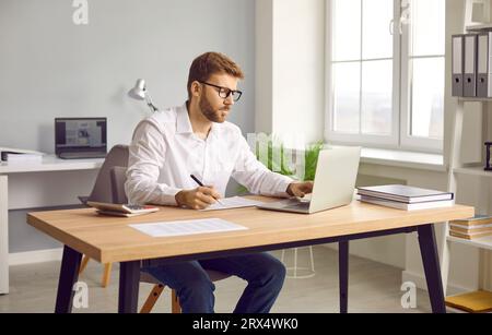 Businessman using laptop and making notes on paper in his office Stock Photo