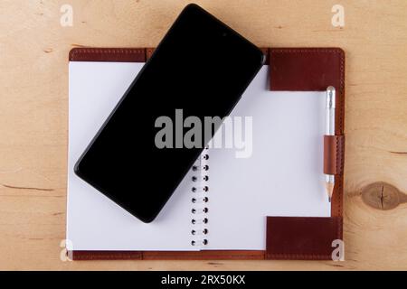 Digitalization concept. Paper notebook vs smartphone. Digital phone with blank black screen and empty  notebook lie on wooden table Stock Photo