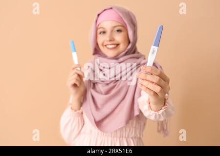 Happy Muslim young woman with positive pregnancy tests on beige background Stock Photo