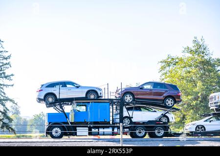 Bright blue industrial car hauler classic carrier big rig semi truck tractor transporting cars and crossovers on hydraulic modular semi trailer drivin Stock Photo