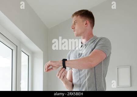 Pensive young man putting on smartwatch when getting ready in the morning Stock Photo