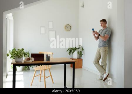 Smiling man leaning on wall on his home office and texting friends and coworkers Stock Photo
