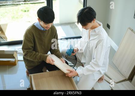 Happy gay couple in new home on moving day and assembling furniture together Stock Photo