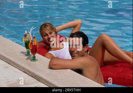 Young couple at the pool, woman lying on air mattress man at the edge of the pool, with cocktail Stock Photo