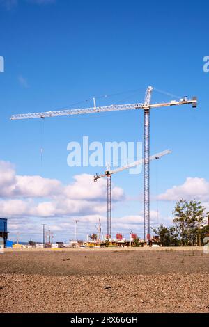 Two. 2 construction cranes on a new building site photographed agaist a blue sky with beautiful puffy clouds. Stock Photo