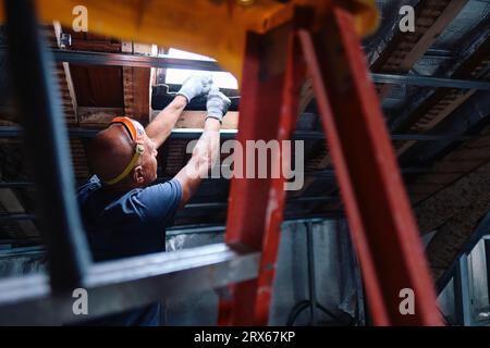 Construction worker repairing ceiling window in attic Stock Photo