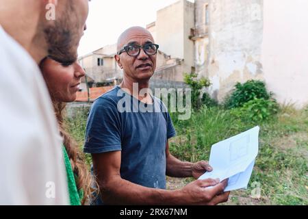 Builder discussing over blueprint with couple at site Stock Photo