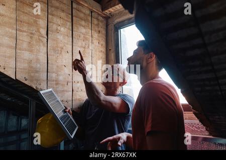 Construction worker holding solar panel and discussing with man at site Stock Photo
