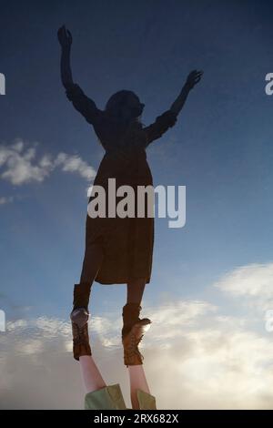 Reflection of woman with arms raised in water puddle Stock Photo