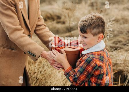 Mother giving gift box to happy son in field Stock Photo