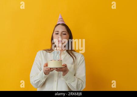 Woman blowing candle on birthday cake against yellow background Stock Photo