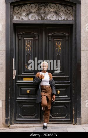 Young businesswoman standing with coffee in front of wooden door Stock Photo
