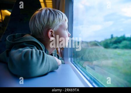 Contemplative blond boy looking through train window Stock Photo