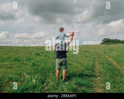 Father carrying son on shoulders and playing in meadow Stock Photo