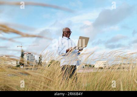 Smiling engineer using laptop in field Stock Photo