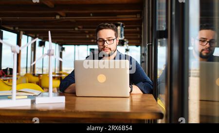 Young engineer with wind turbine models using laptop at table Stock Photo