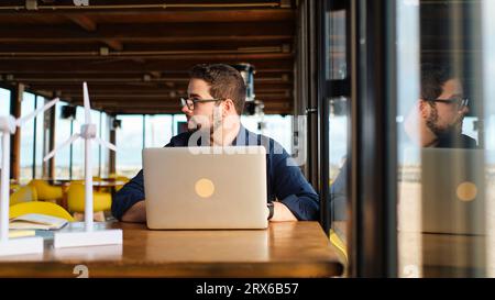 Young engineer sitting with wind turbine models and laptop at table Stock Photo