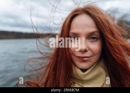 Redhead woman with long hair by lake Stock Photo