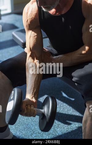 Strong man exercising with dumbbell in health club Stock Photo