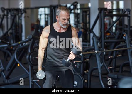 Strong mature man doing exercise with dumbbells in gym Stock Photo