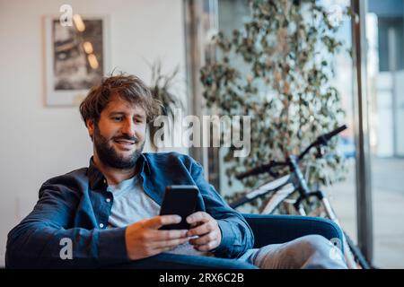 Smiling businessman using smart phone in office Stock Photo