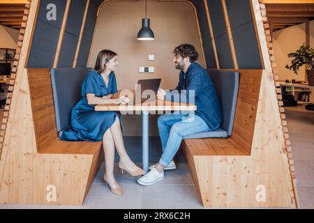 Happy business people sitting with laptop and talking in office cubicle Stock Photo